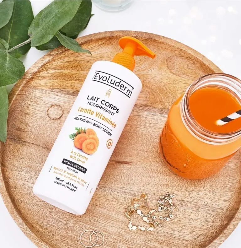 Lotion nourrissante Evoluderm à la carotte vitaminée sur un plateau en bois avec un verre de jus de carotte et des bijoux.