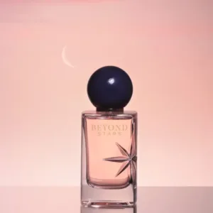 Flacon de parfum “BEYOND STARS” avec bouchon sphérique foncé, sur fond dégradé rose.