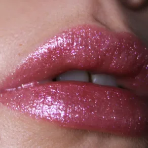 Lèvres avec du brillant à lèvres rose scintillant, montrant une texture lisse et brillante avec des reflets lumineux.